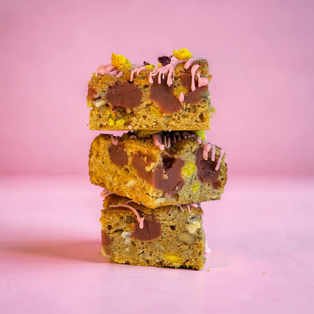 Brownies with pink drizzle and yellow and purple decorations