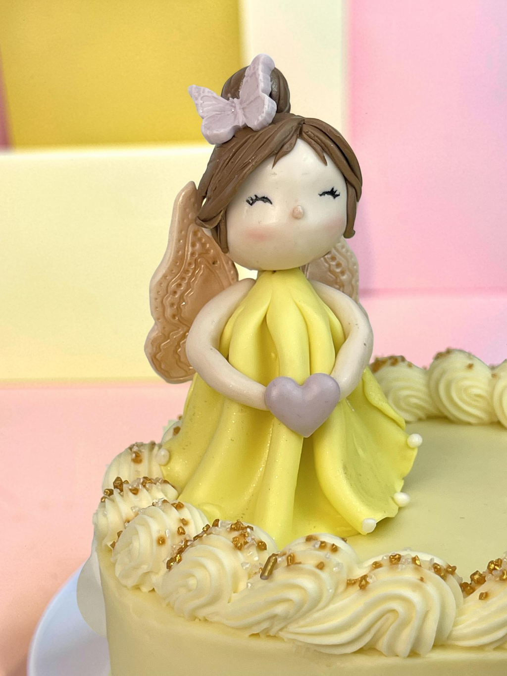 Cake topper of a girl in a yellow dress with a heart, on a cake with white frosting and gold accents.