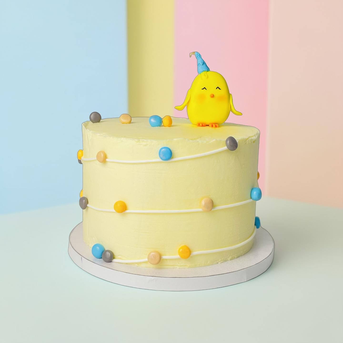 Yellow cake with colorful polka dots and a small yellow chick figurine on top against a pastel background