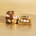 Two cookie dough balls with chocolate and marshmallow filling on a gold background